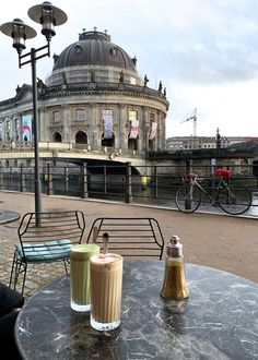 two drinks are sitting on an outdoor table in front of a building with a river running through it