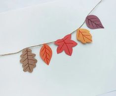 paper leaves are hanging from a string on a white surface with brown and orange colors