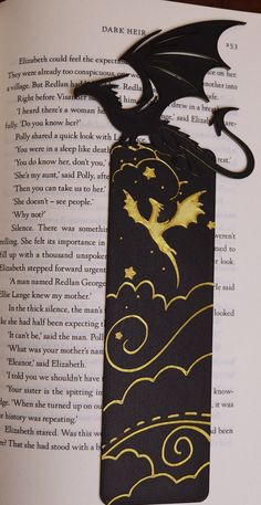 an open book with a black and gold dragon on it's cover, in the shape of a bookmark