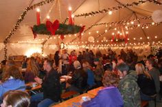 a large group of people sitting at tables in a tent with lights on the ceiling