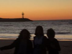 three people walking on the beach at sunset