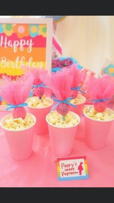 pink cups filled with popcorn sitting on top of a table next to a happy birthday sign