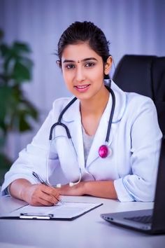 a female doctor sitting at her desk in front of a laptop computer with a stethoscope on it