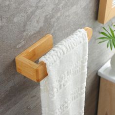 a bamboo towel rack on the wall next to a white vase with a green plant in it