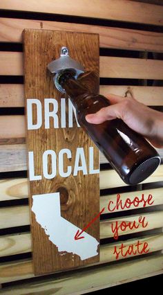 a person holding a beer bottle in front of a wooden sign