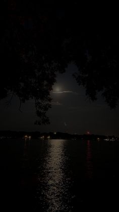 the moon shines brightly in the dark night sky over water with trees and lights