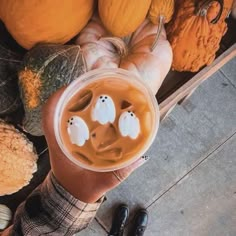 a person is holding a cup with liquid in it and some pumpkins behind them