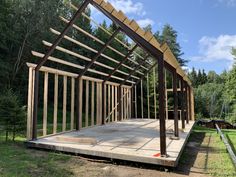 a wooden structure is being built in the middle of a field with trees behind it