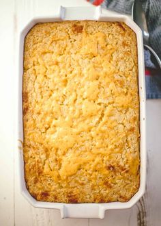 a casserole dish with cheese in it on a white table next to a spoon