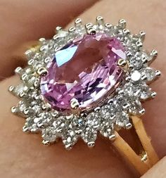 a woman's hand holding a ring with an oval shaped pink stone surrounded by white and yellow diamonds