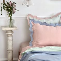 a bed with pink, blue and green pillows next to a white table holding flowers