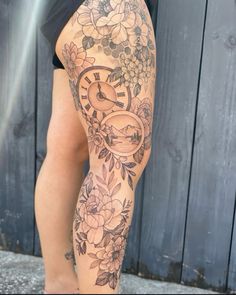 a woman's leg with flowers and a clock tattoo on her arm, next to a wooden fence