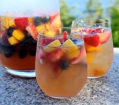 three glasses filled with fruit and ice on top of a stone table next to trees