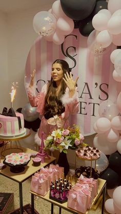 a woman standing in front of a table filled with cakes and cupcakes