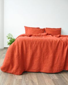 an orange bed with two pillows on it and a plant in the corner next to it