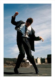 a man in a suit and tie is doing a trick on a skateboard outside