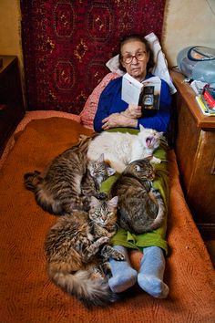 an old woman is reading a book with her cats