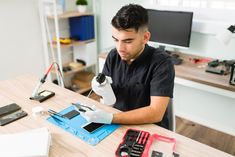 a man sitting at a table working on something with a microscope in front of him