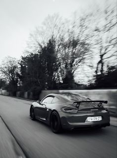 a grey sports car driving down the road with trees in the background