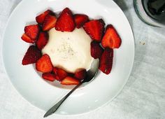 a white plate topped with strawberries covered in cream sauce and a spoon on top of it