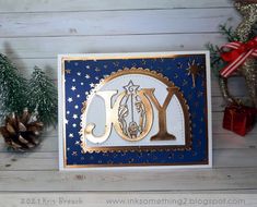 a christmas card with the word joy in gold and blue, surrounded by pine cones