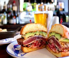 a cut in half sandwich sitting on top of a white plate next to a glass of beer