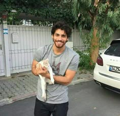 a man is holding a white cat in his hands while standing next to a car