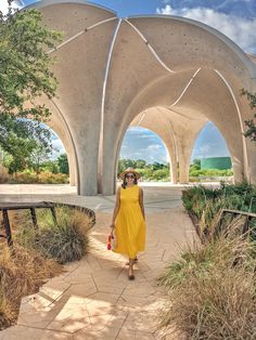 a woman in a yellow dress is walking down a walkway with arches and grass on either side