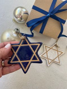 a hand holding a star of david ornament in front of a gift box