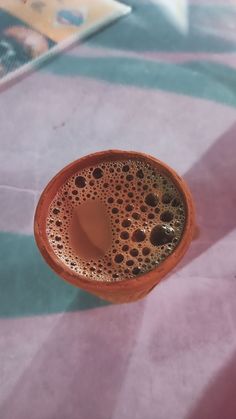 there is a small cup with some liquid in it on the tablecloth, next to a book