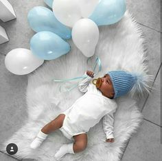 a baby is laying on a white rug with blue and white balloons in the background