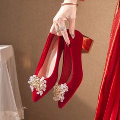 a woman's hand holding two pairs of red high heels with pearls on them