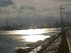 the sun shines brightly in front of water and power lines on an overcast day