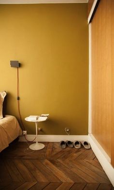 a bedroom with yellow walls and wooden flooring, an ironing board on the wall