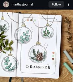 an open planner with christmas ornaments and greenery on it, next to some pens