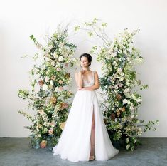 a woman in a wedding dress standing next to an arch of flowers and greenery