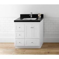 a bathroom vanity with black counter top and white cabinetry in front of a brick wall