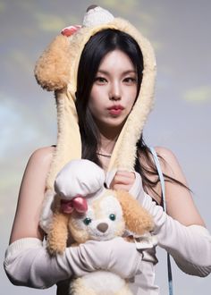 a woman holding a teddy bear wearing a hood over it's head and covering her face