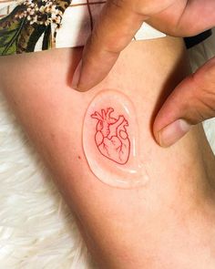 a person with a red heart tattoo on their leg and the other hand is touching it