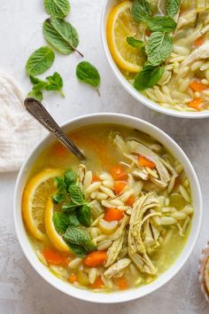 two bowls of chicken noodle soup with lemons, carrots and mint leaves