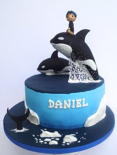 a birthday cake decorated with two orca whales and a boy on the top tier