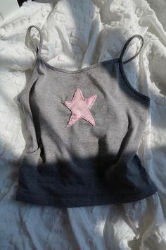 a gray and pink top with a star on the front sitting on a white sheet