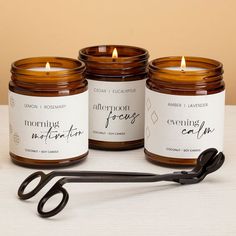 three amber glass jar candles lit on a table with a wick trimmer Candle Labels Ideas, Relax Candle, Scented Candles Packaging, Soy Candle Business, Prosperity Candle, Wellness Candles, Candle Labels Design, Healing Candles