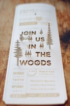 a wooden table topped with a paper cut out of trees and the words join us in at the woods