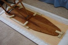 a wooden surfboard sitting on top of a white mat in a room with carpet