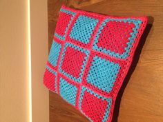 a red and blue crocheted cushion sitting on top of a wooden floor