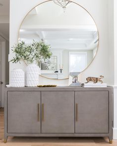 a large round mirror on top of a gray cabinet in a white room with wood floors