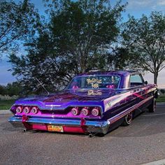 an old purple car is parked on the side of the road with trees in the background