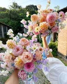 a bouquet of flowers being held up by two hands in front of a brick building