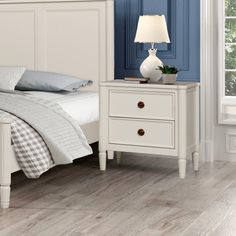 a white bed sitting next to a night stand on top of a hard wood floor